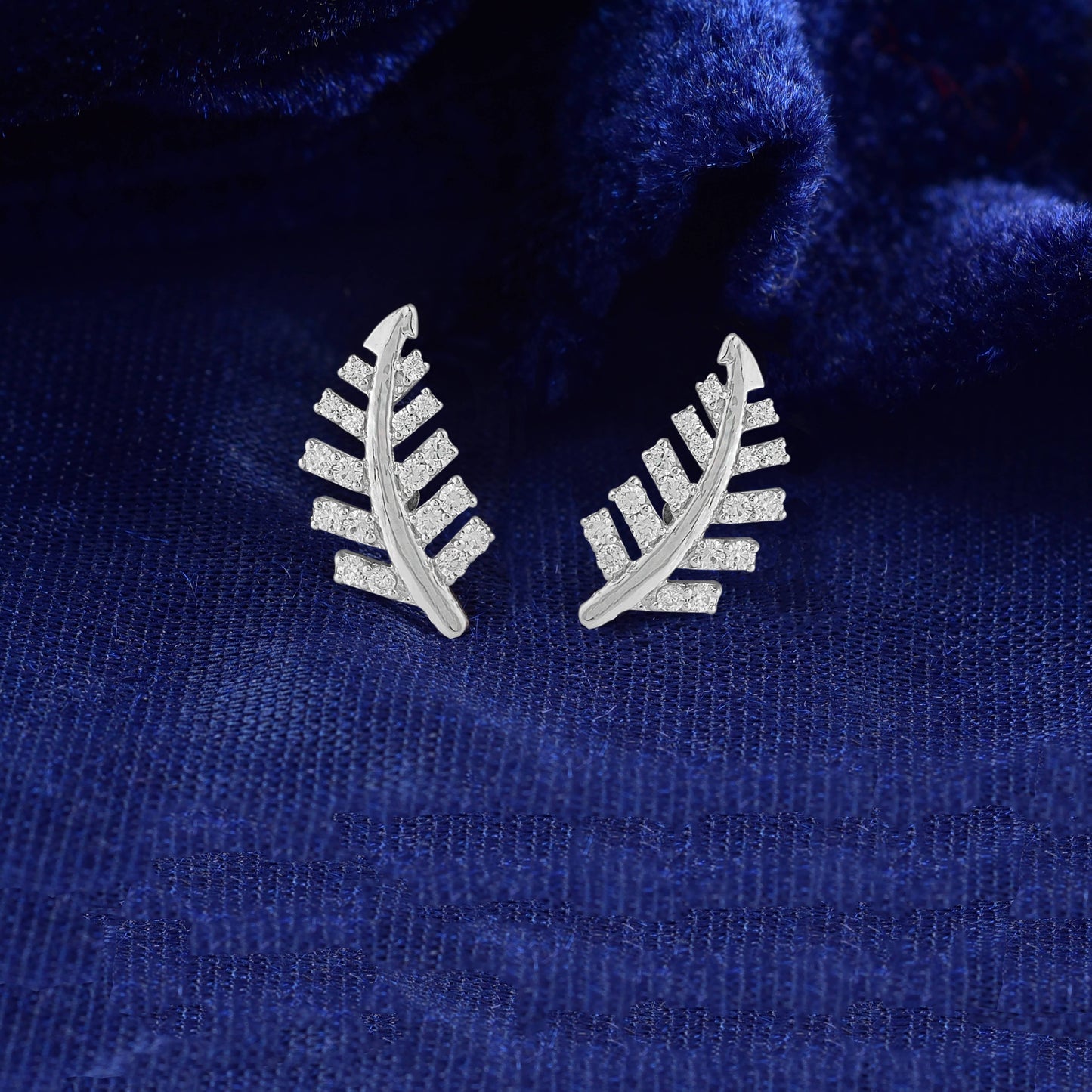 Pair of leaf-shaped earrings on a blue textured fabric background