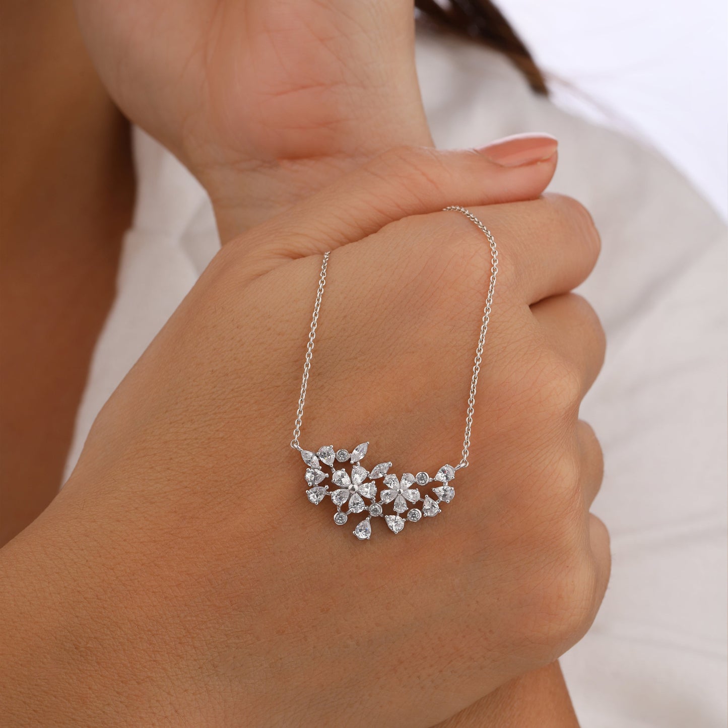 Silver necklace with a floral pendant held in a hand against a neutral background