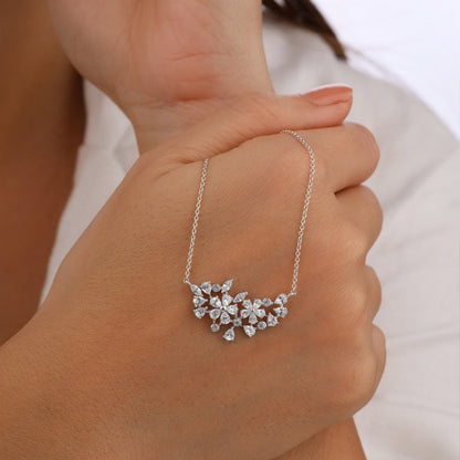 Silver necklace with a floral pendant held in a hand against a neutral background