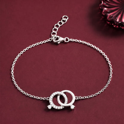 A silver chain bracelet with a double interlocking ring charm set with small clear stones