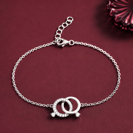 A silver chain bracelet with a double interlocking ring charm set with small clear stones