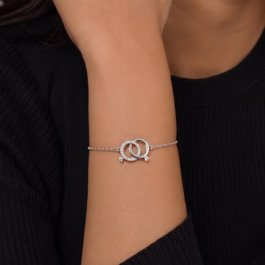 silver chain bracelet with a double interlocking ring charm, one of which is set with small clear stones