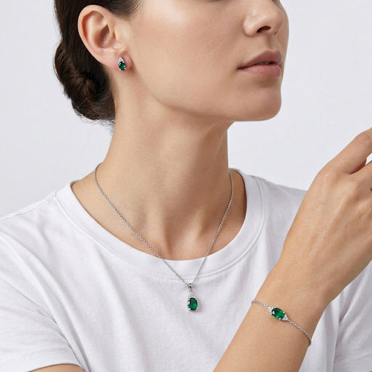 Woman wearing a silver necklace, earrings, and bracelet with green gemstones 