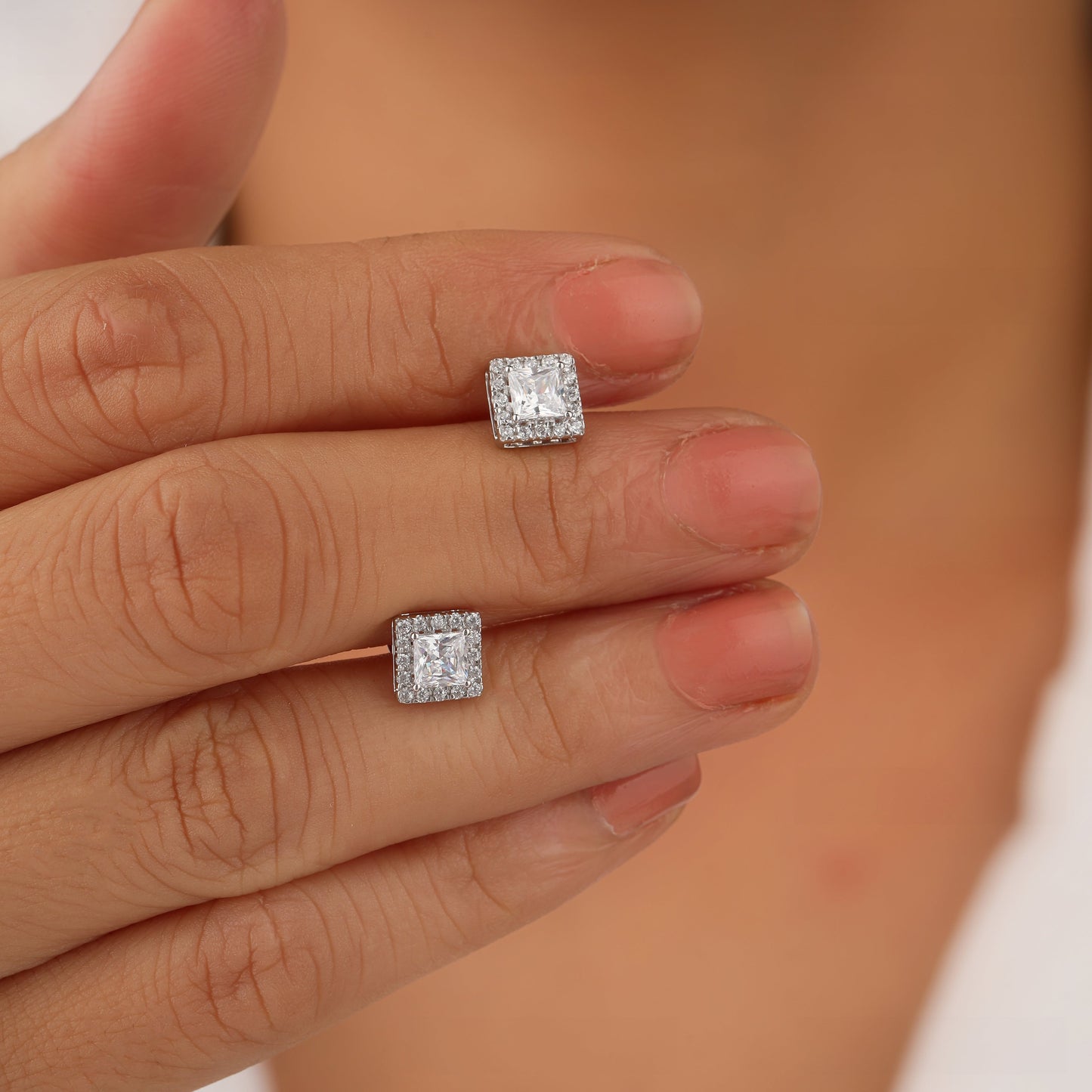 Square-shaped diamond earrings on a hand with a blurred background