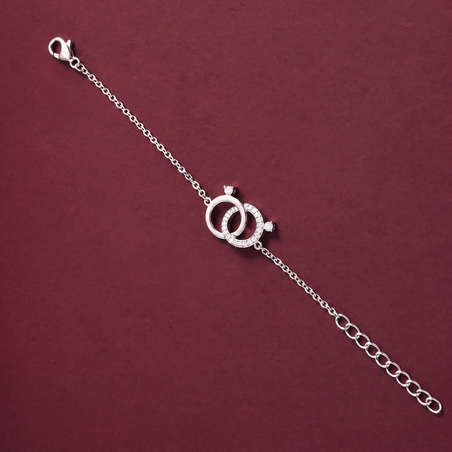A silver chain bracelet featuring two interlocking rings with small clear stones