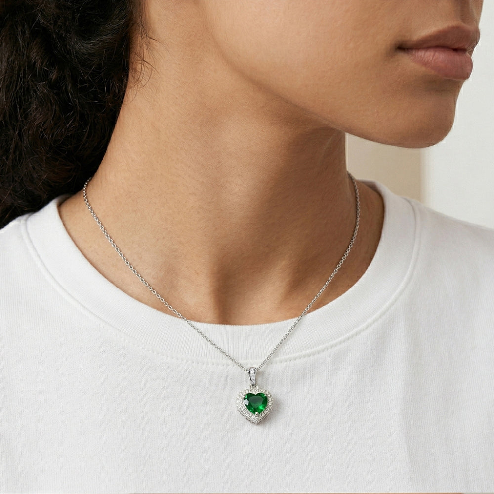 Person wearing a silver necklace with a heart-shaped green gemstone pendant.