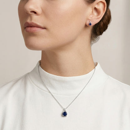 Woman wearing a silver necklace with a blue pendant and matching earrings 