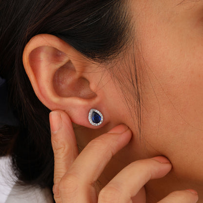 Close-up of an ear wearing a blue gemstone earring with a hand adjusting it.