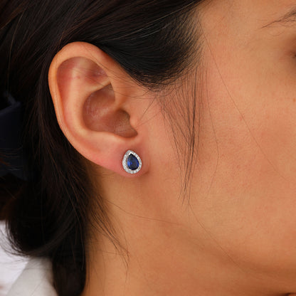 Close-up of an ear wearing a blue gemstone earring with a blurred background