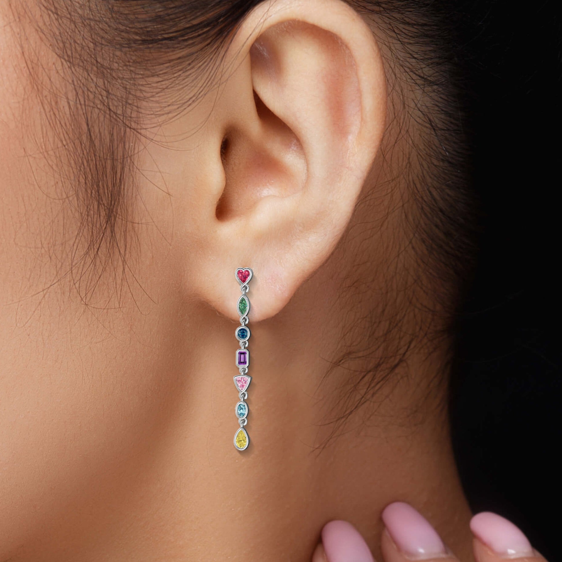 Close-up of an ear wearing a colorful earring with a hand adjusting it against a dark background.