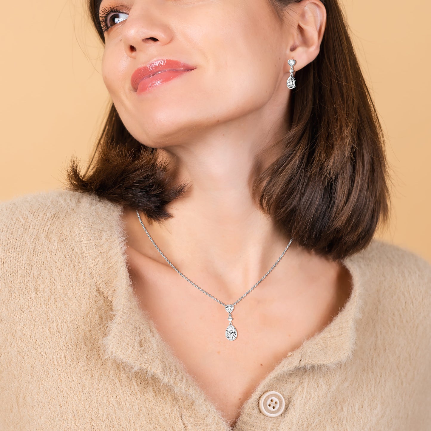 Woman wearing a silver necklace and earrings against a beige background